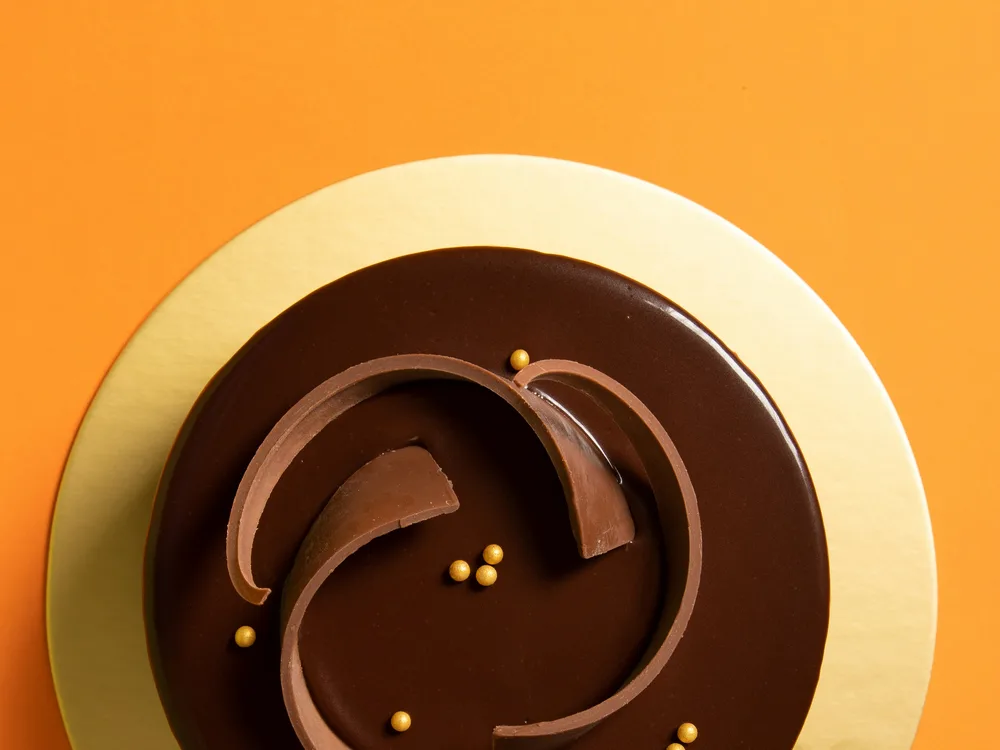A chocolate mirror-glaze cake with curled chocolate shards on a gold board