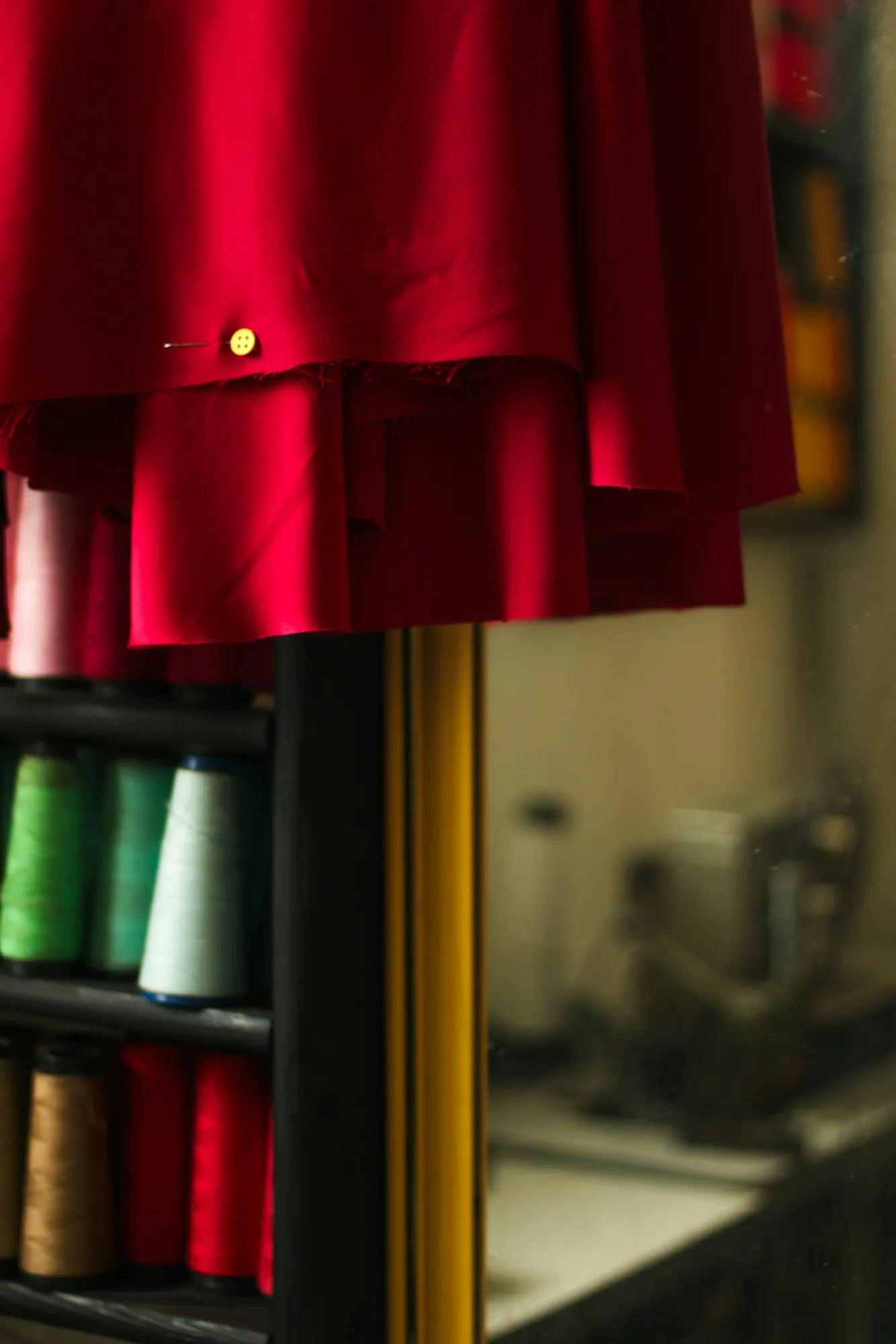A red dress on a rail beside shelves of coloured thread