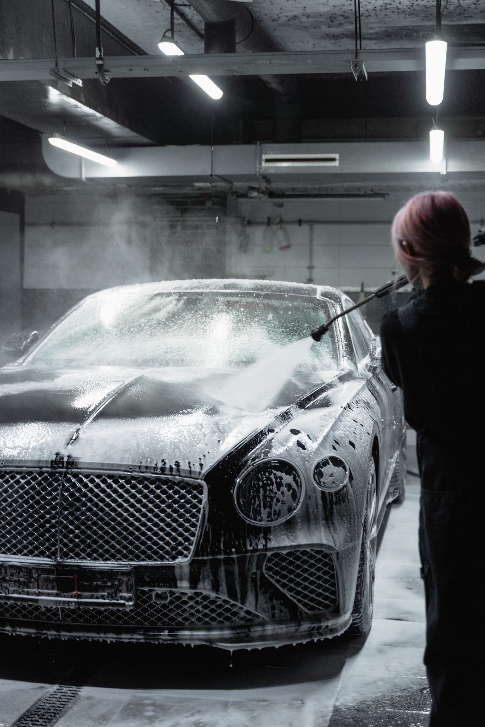 A dark car under pressure-washed foam in a detailing bay